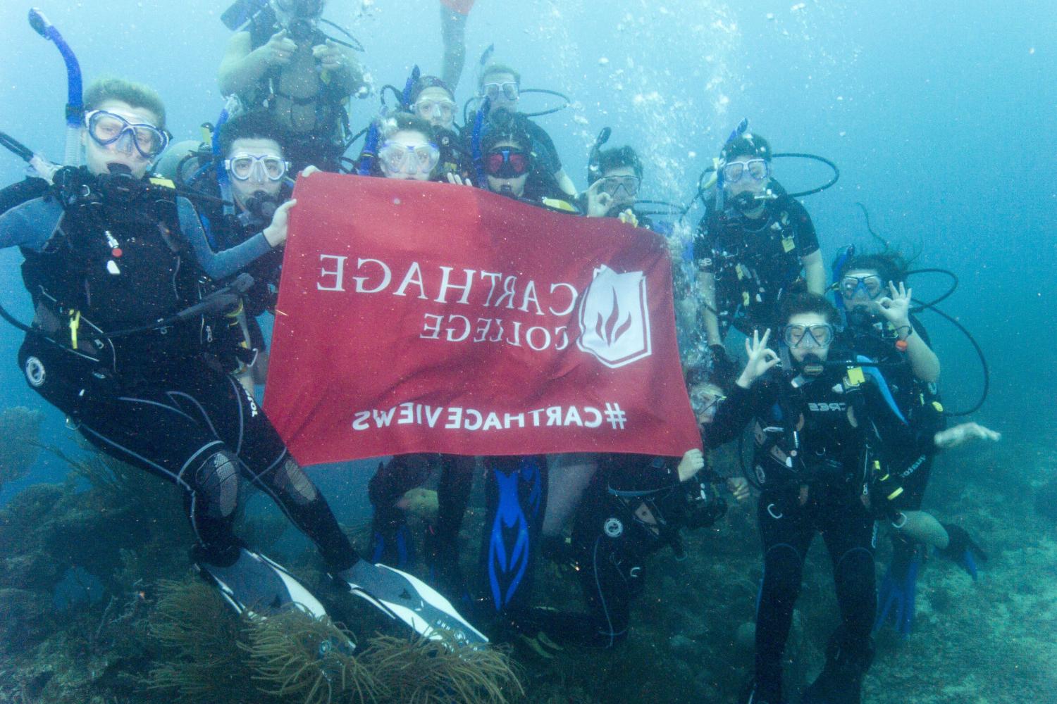 学生们手持<a href='http://jp.bjrujiabj.com/'>博彩网址大全</a>旗帜，在j学期洪都拉斯游学之旅中潜水.